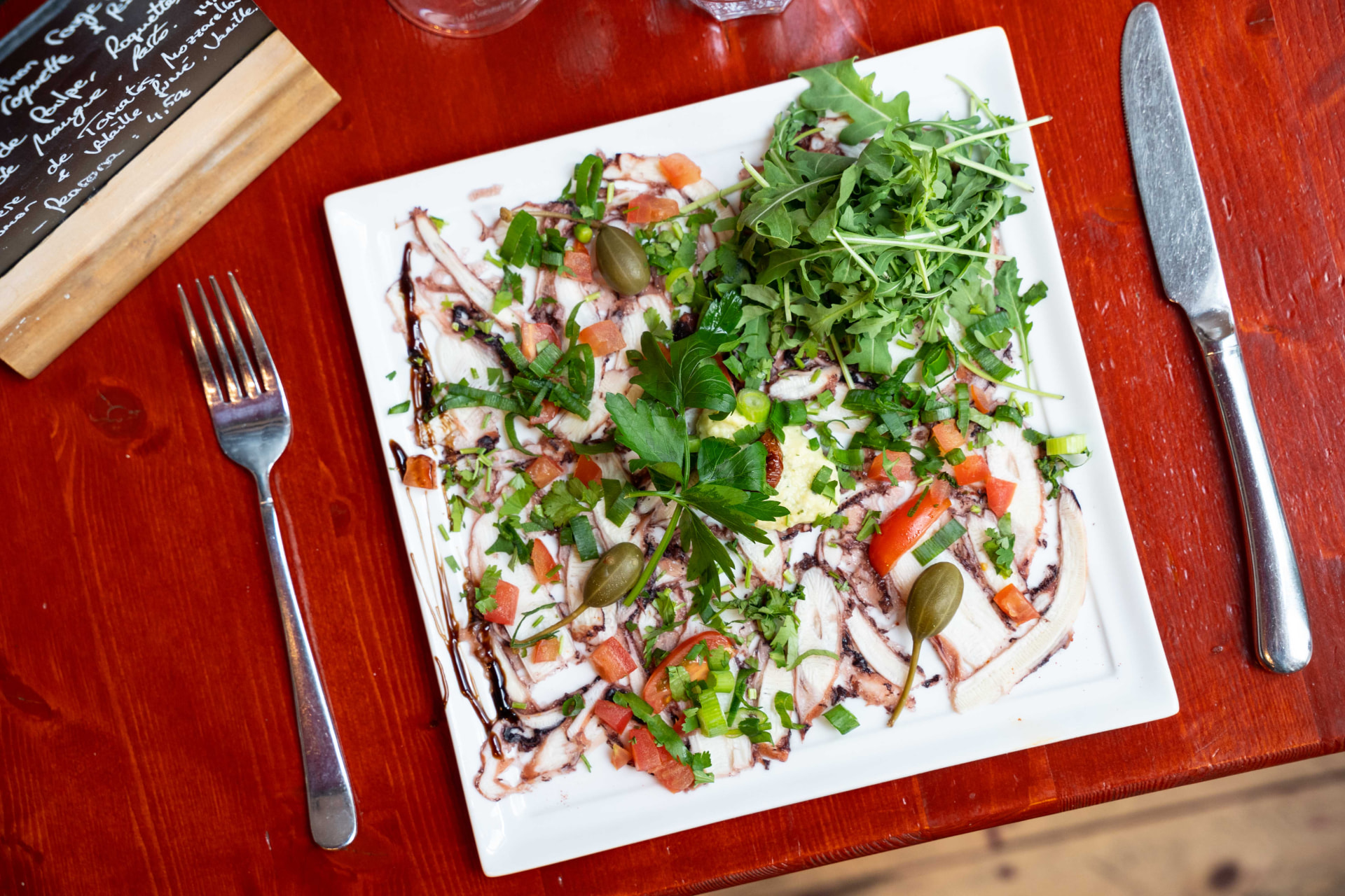 Carpaccio de poulpe vu de dessus sur table en bois rouge du restaurant